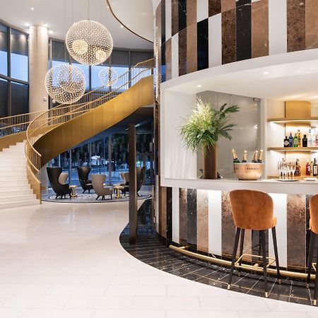 Eurostars Universal Lisboa Dış mekan fotoğraf The photo depicts a stylish, modern interior space featuring a curved staircase with a golden railing. The staircase leads to an upper level and is illuminated by large pendant lights. To the right, there is a sleek bar area with a white countertop, 