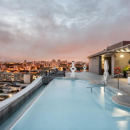Eurostars Universal Lisboa Dış mekan fotoğraf The photo shows a rooftop pool with a modern design, featuring clear blue water and a sleek edge that appears to blend into the skyline. In the background, there are city buildings illuminated by sunset colors, giving the scene a warm and inviting at