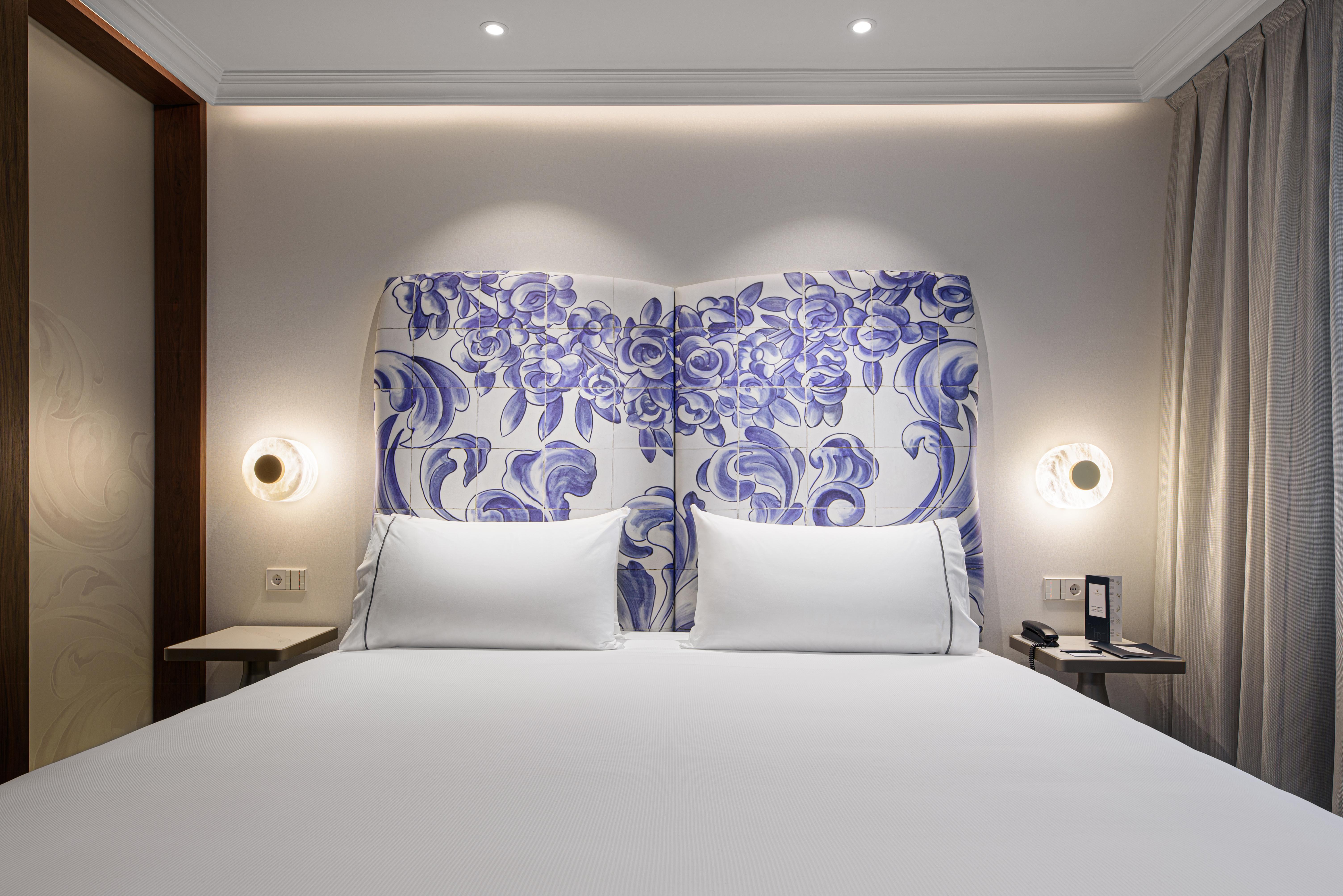Eurostars Universal Lisboa Dış mekan fotoğraf The photo shows a well-decorated hotel room with a focus on the bed. The bed has a decorative headboard featuring a blue and white floral pattern. There are two neatly arranged white pillows on the bed. On either side of the headboard, there are mode