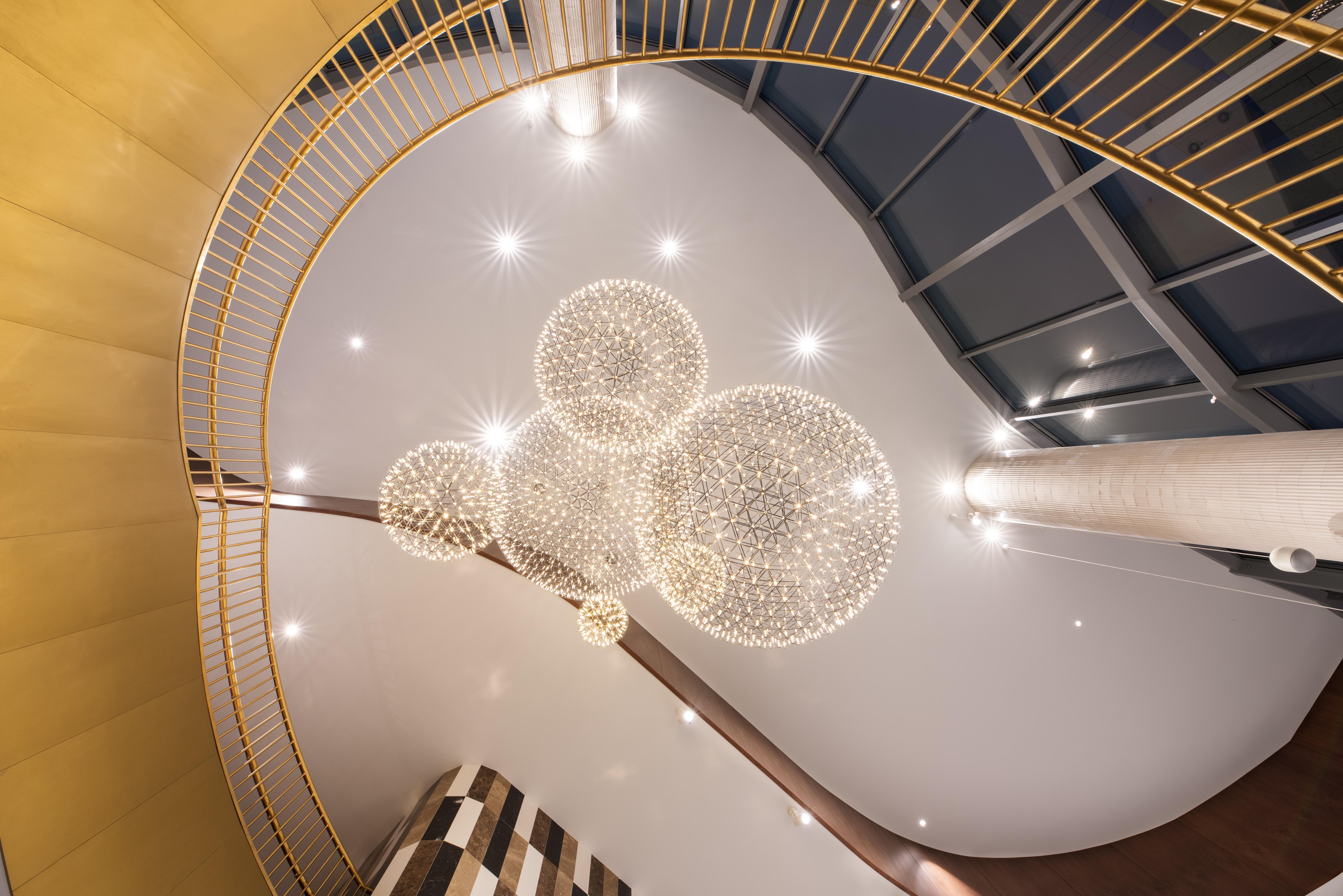 Eurostars Universal Lisboa Dış mekan fotoğraf The photo shows an interior space viewed from below, showcasing a spiraling staircase with a golden railing. Above, there are several elegant spherical chandeliers that emit soft, ambient light. The ceiling is smooth and features recessed lighting, c