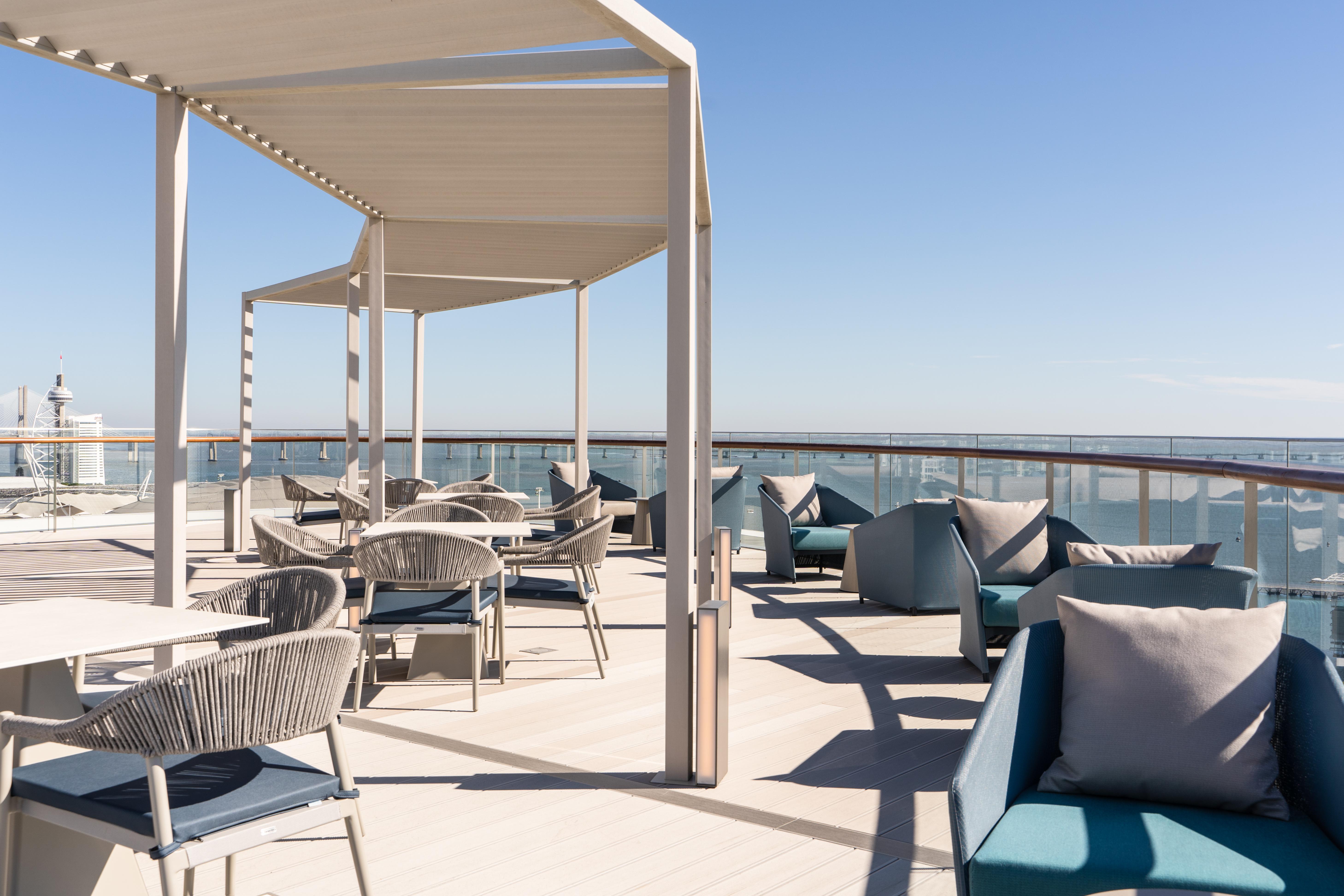 Eurostars Universal Lisboa Dış mekan fotoğraf The photo shows a spacious outdoor seating area on a deck or terrace. There are several stylish chairs and tables arranged under a white canopy for shade. The furniture appears contemporary, with a mix of materials including woven textures. The backd