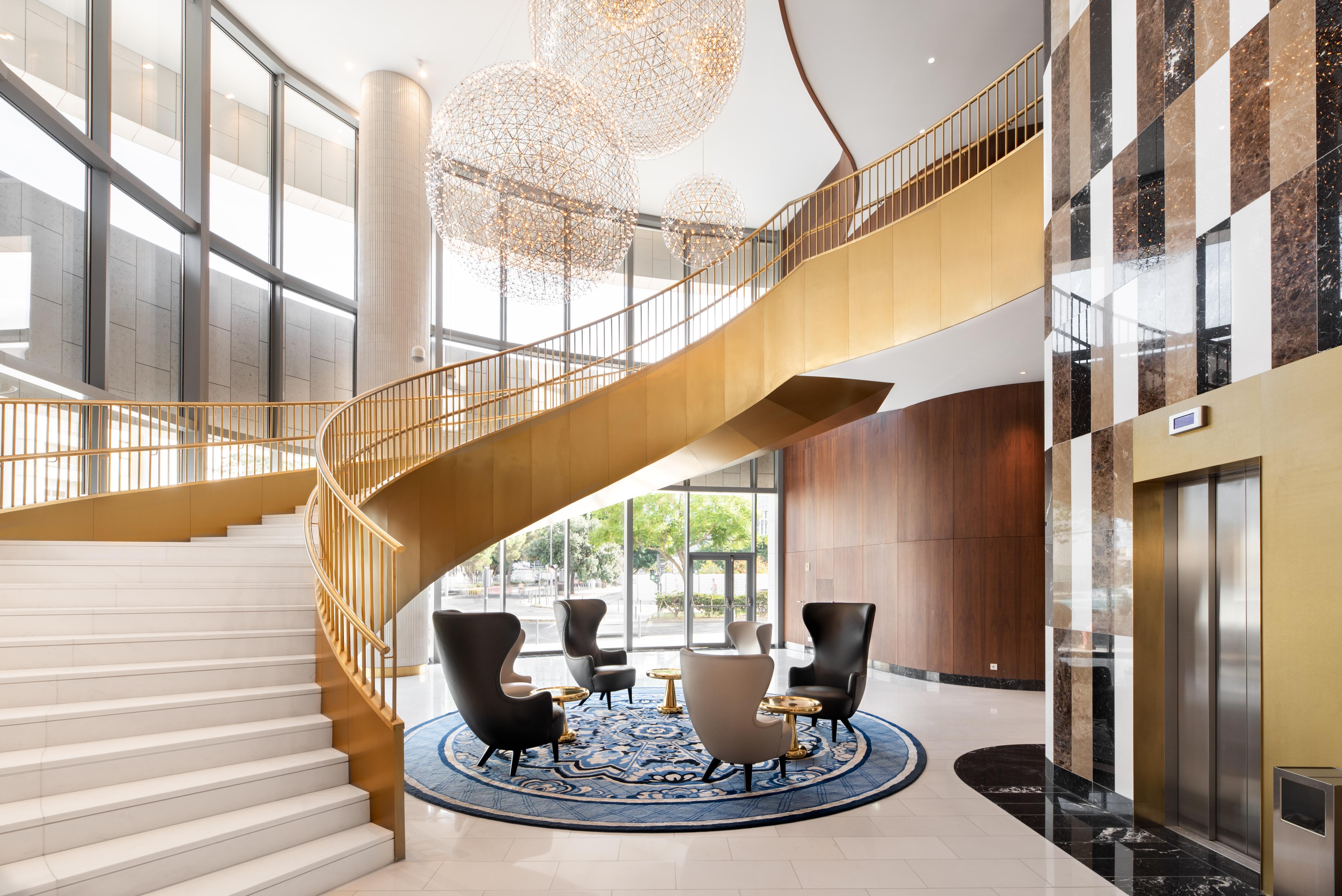 Eurostars Universal Lisboa Dış mekan fotoğraf The photo showcases an elegant lobby area featuring a grand staircase with a delicate, curved design and a golden railing. The staircase is flanked by a set of luxurious black armchairs arranged around a round table, all placed on an ornate blue rug.