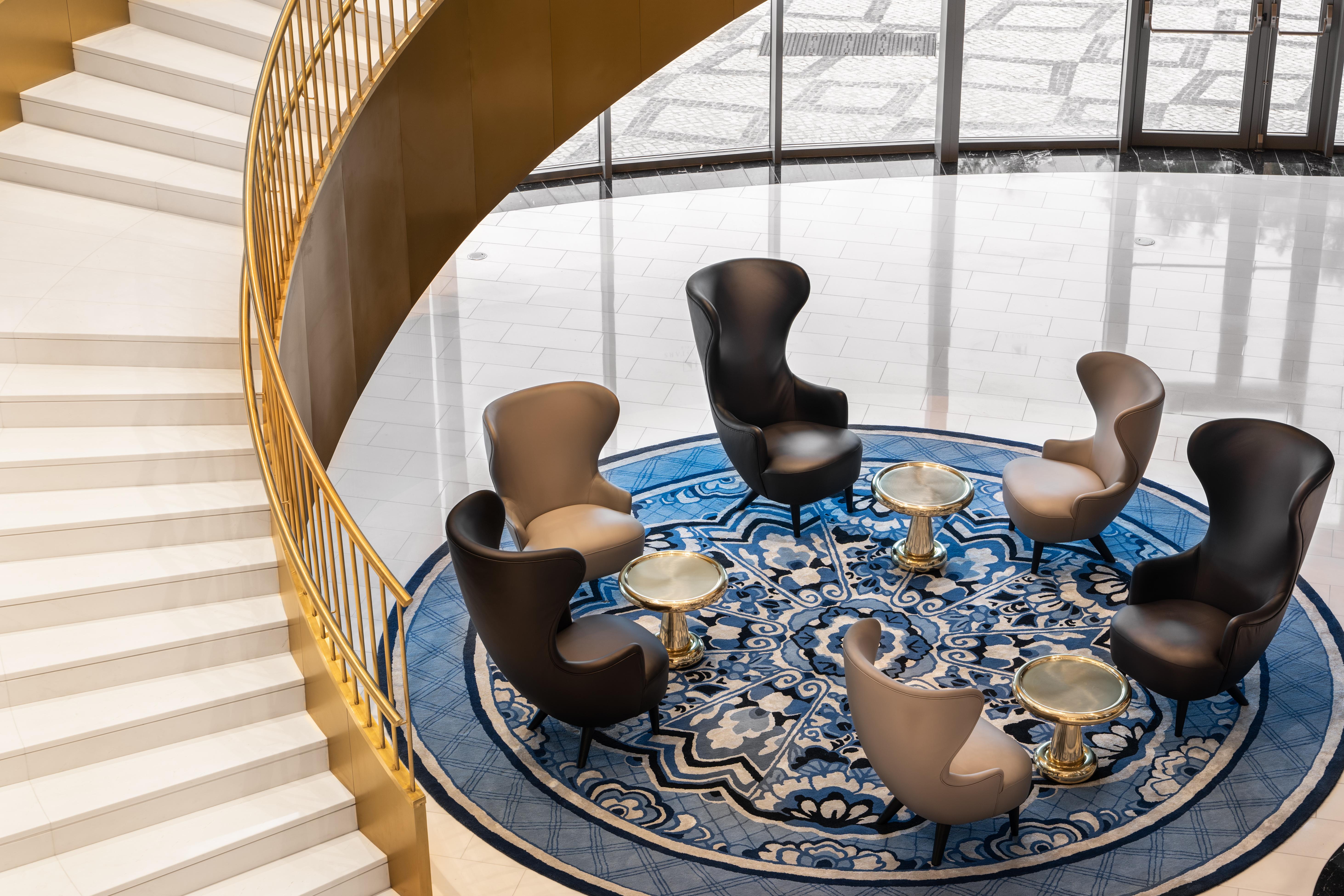 Eurostars Universal Lisboa Dış mekan fotoğraf The photo shows a stylish lounge area featuring an elegant, modern design. In the center, there is a round blue rug with intricate patterns. Surrounding the rug are several contemporary chairs in various colors—two in light beige and two in black. Sm