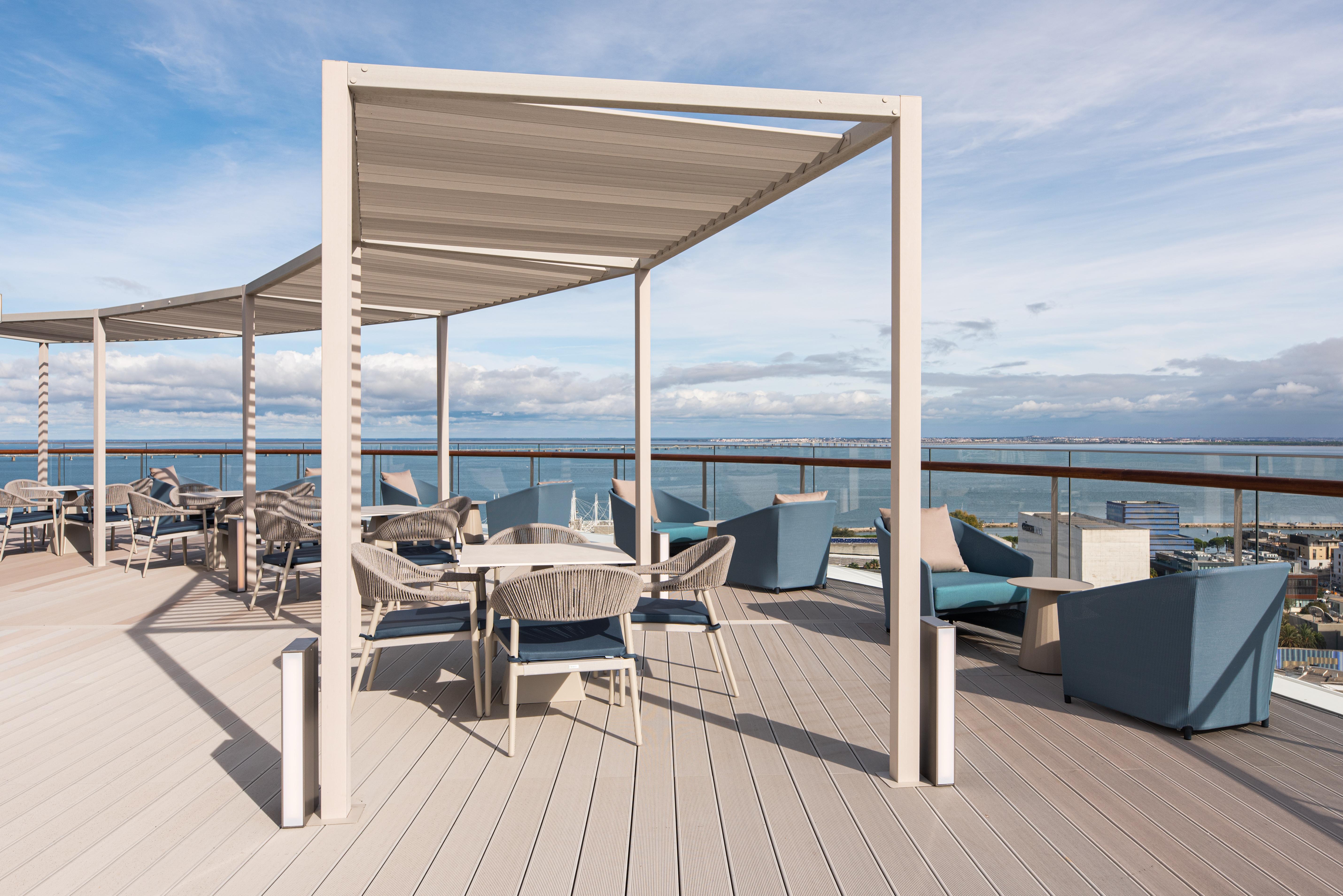 Eurostars Universal Lisboa Dış mekan fotoğraf The photo shows a modern rooftop terrace with a spacious deck. There are several outdoor seating areas equipped with stylish furniture, including tables and chairs. A large, shaded structure provides cover for some of the seating. In the background, 