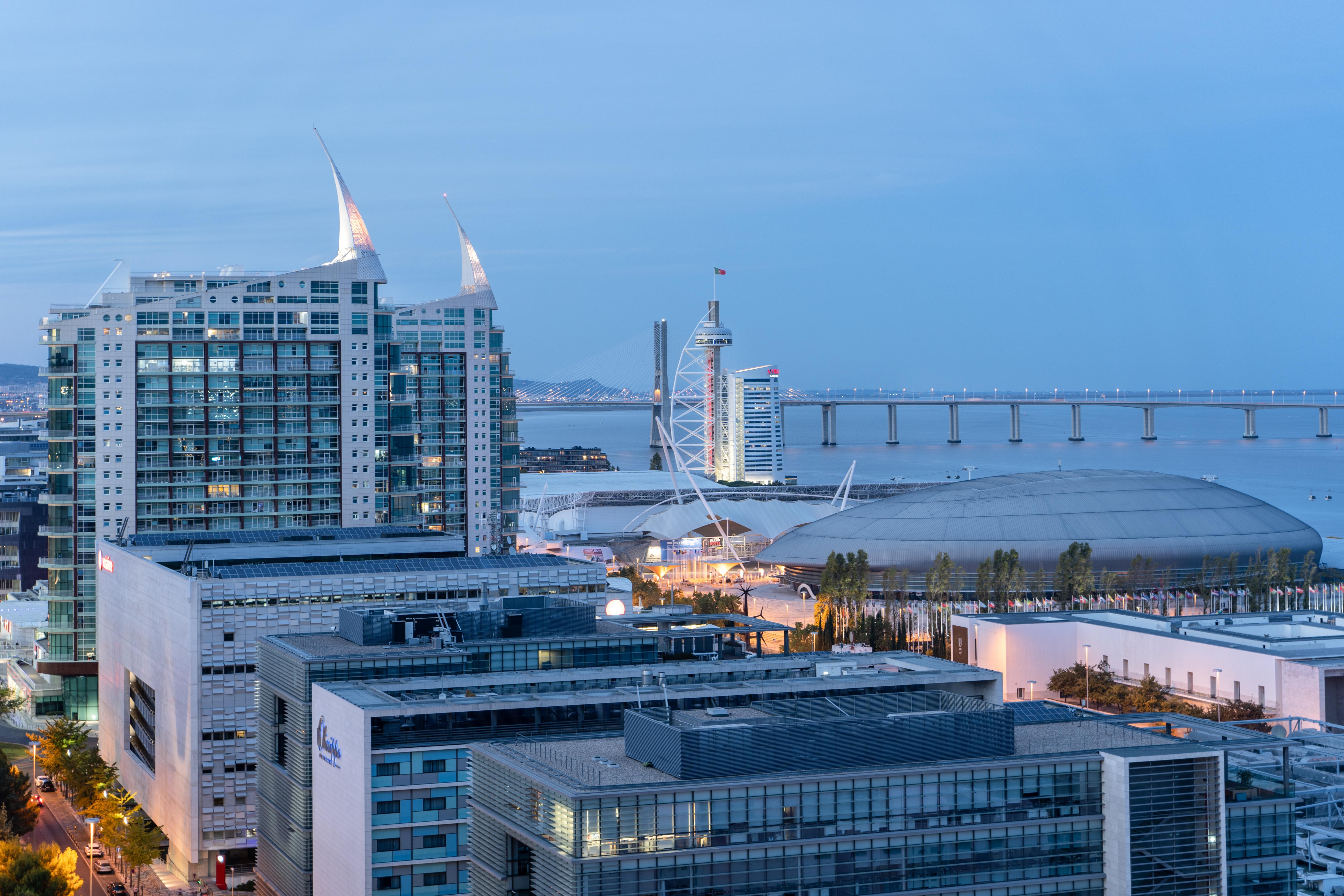 Eurostars Universal Lisboa Dış mekan fotoğraf The photo depicts a modern urban landscape at dusk, showcasing a combination of tall buildings and structures. In the foreground, there's a cluster of contemporary architecture, including large glass buildings with a sleek design. In the background, 