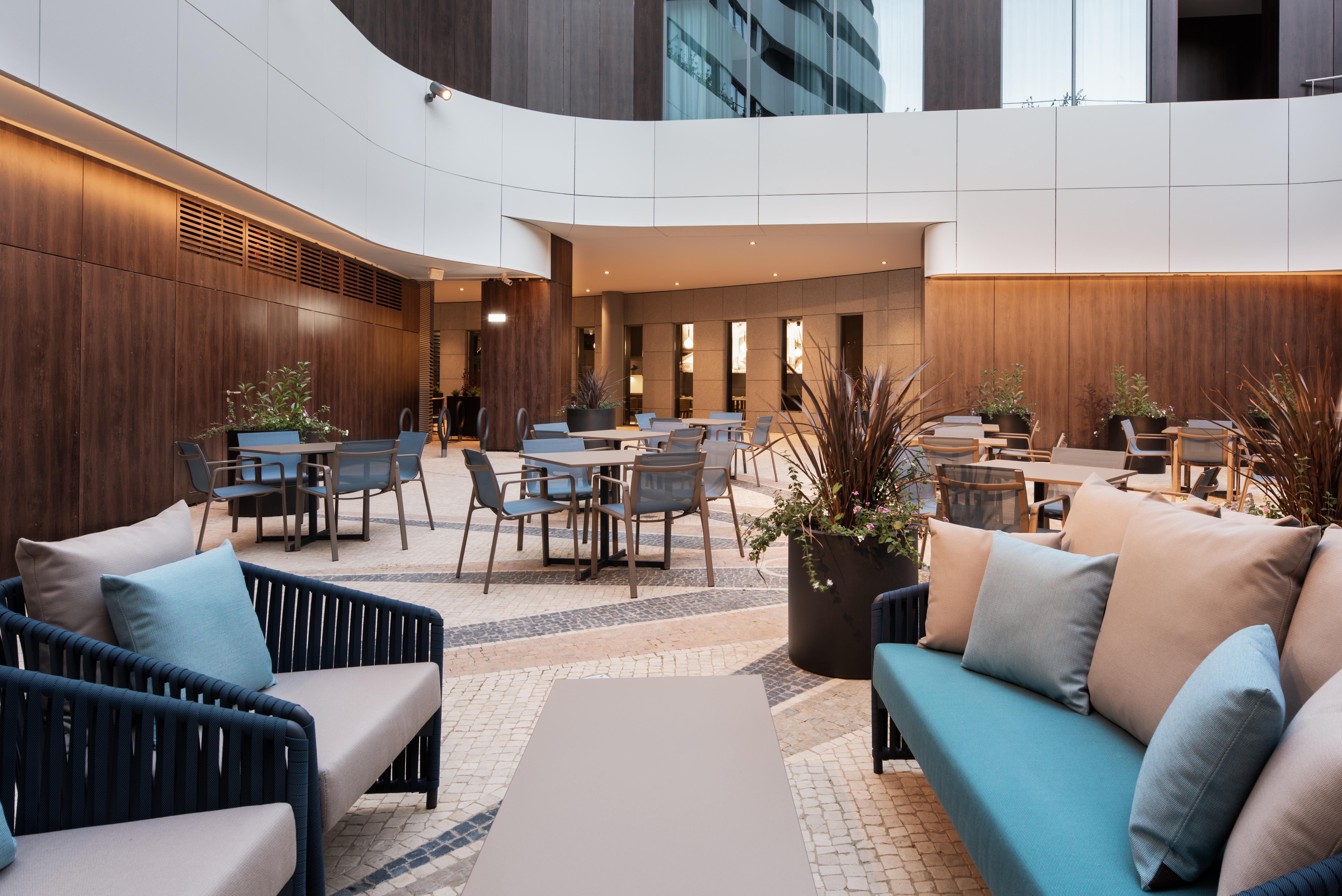 Eurostars Universal Lisboa Dış mekan fotoğraf The photo shows a modern outdoor seating area that features a combination of lounge and dining furniture. There are several stylish tables and chairs arranged throughout the space, surrounded by planters with greenery. The seating consists of comfort