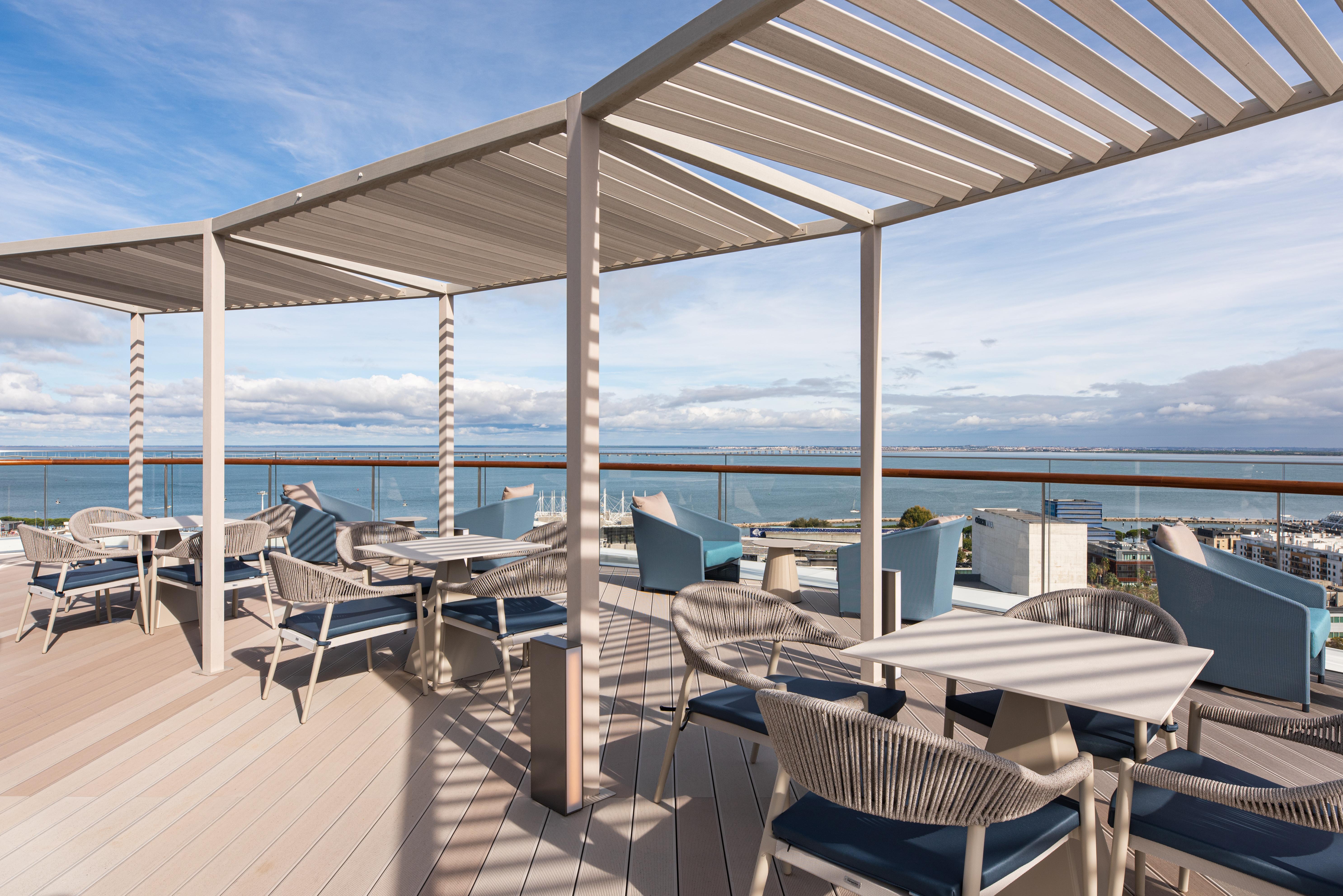 Eurostars Universal Lisboa Dış mekan fotoğraf The photo shows a stylish outdoor terrace or rooftop area. There are several tables and chairs arranged neatly on a wooden floor, with comfortable seating that includes woven chairs. A pergola provides some shade, and the design incorporates clean li