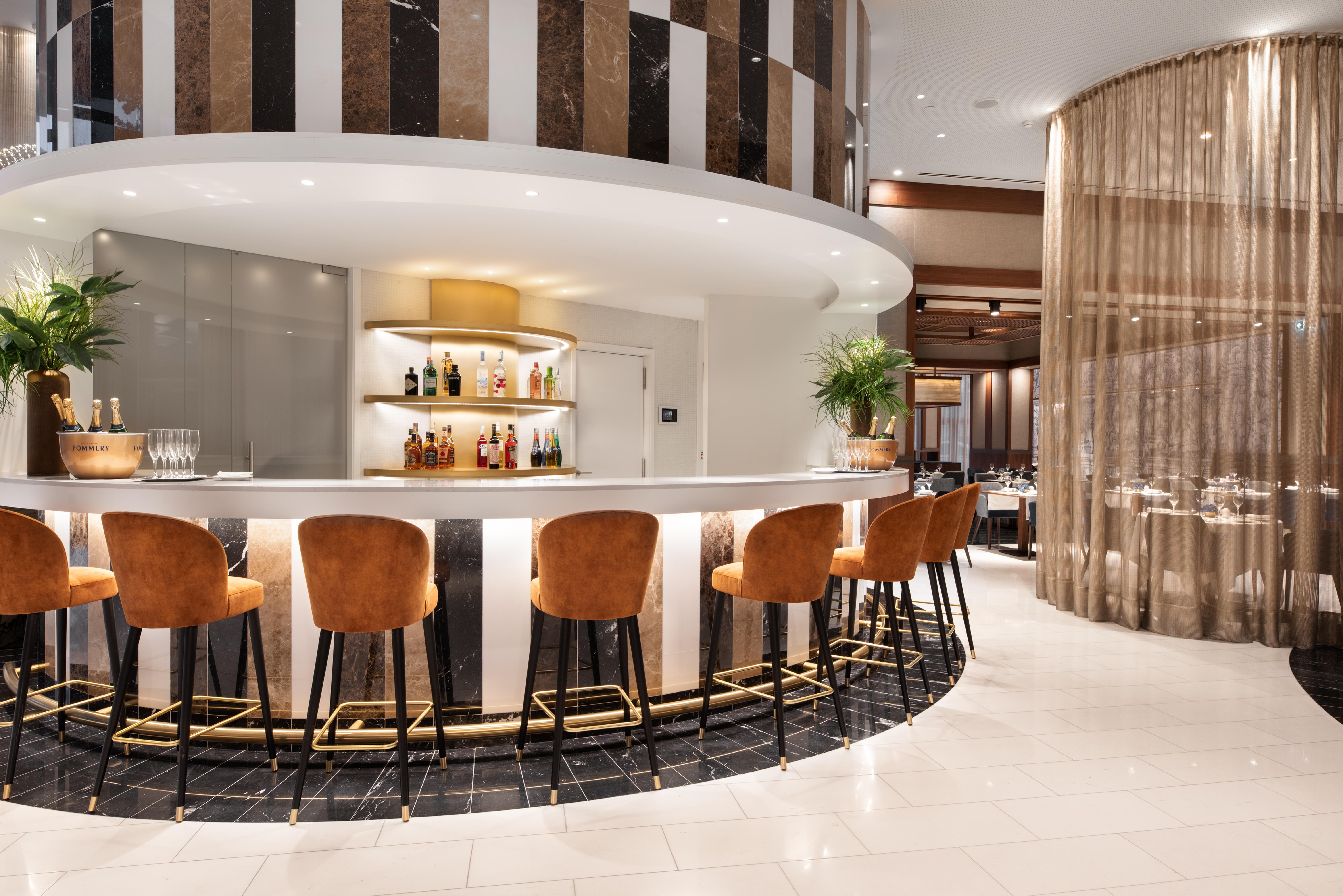 Eurostars Universal Lisboa Dış mekan fotoğraf The photo shows a stylish bar area within a modern restaurant. The circular bar features a sleek countertop and has several high chairs with brown upholstery. Behind the bar, there are shelves displaying a variety of liquor bottles, complemented by s