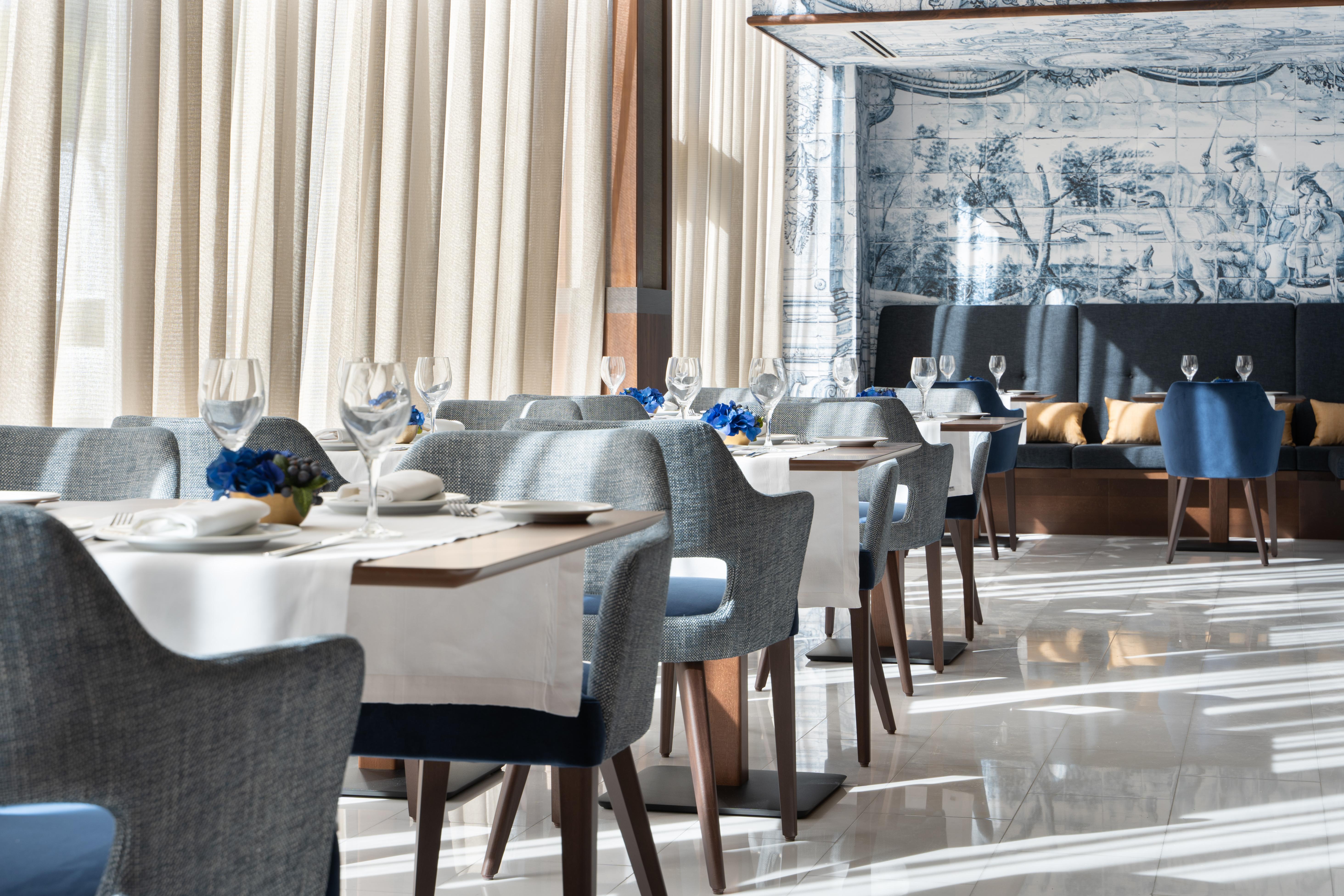 Eurostars Universal Lisboa Dış mekan fotoğraf The photo shows an elegant restaurant interior. It features modern dining tables set with white tablecloths and neatly arranged tableware, including wine glasses. The chairs are upholstered in a soft gray fabric, and there are decorative elements lik