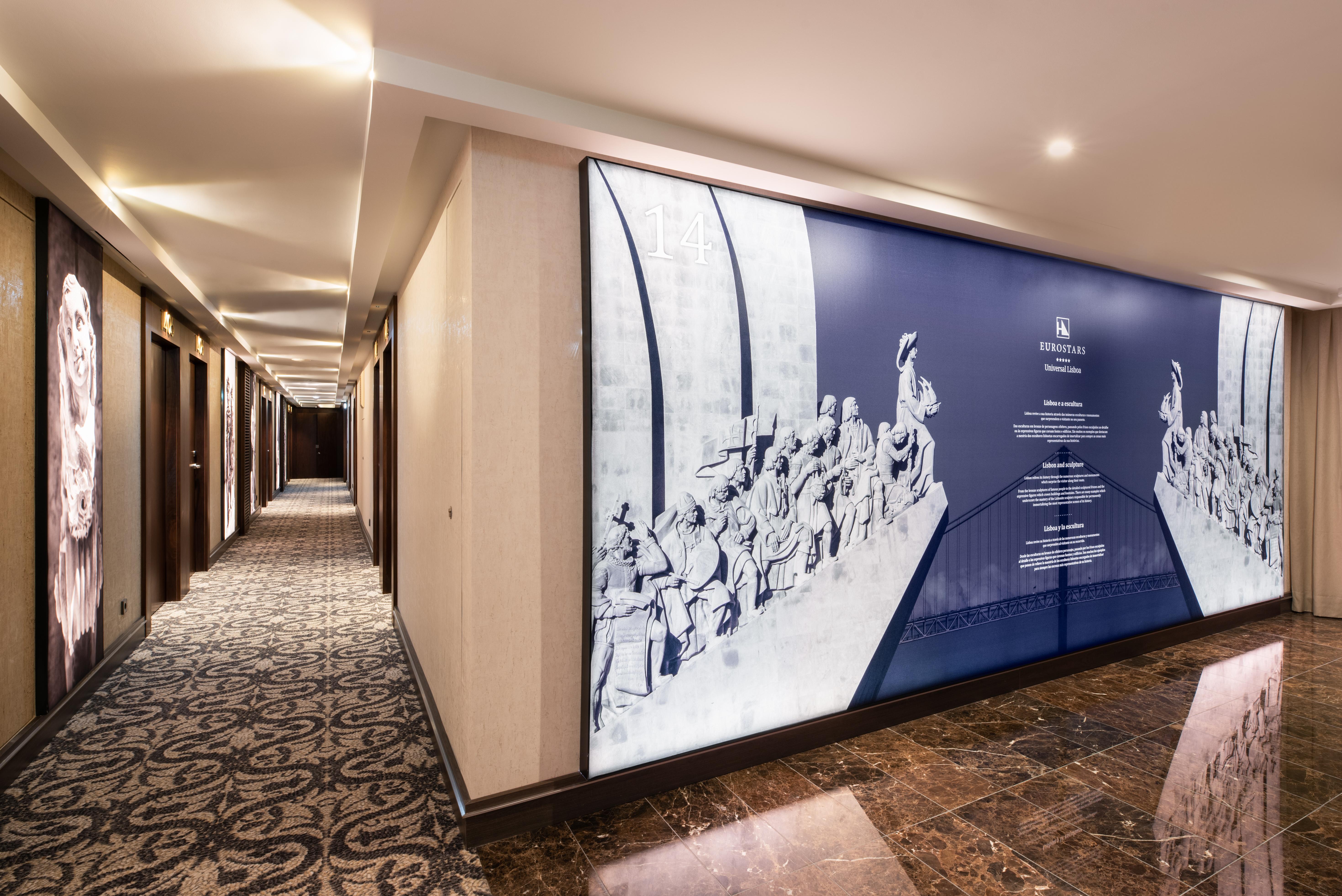 Eurostars Universal Lisboa Dış mekan fotoğraf The photo shows a dimly lit hallway in a hotel or building. It features a series of doors on both sides of the corridor, which likely lead to guest rooms or offices. On one side of the hallway, there is a large decorative wall display that features a