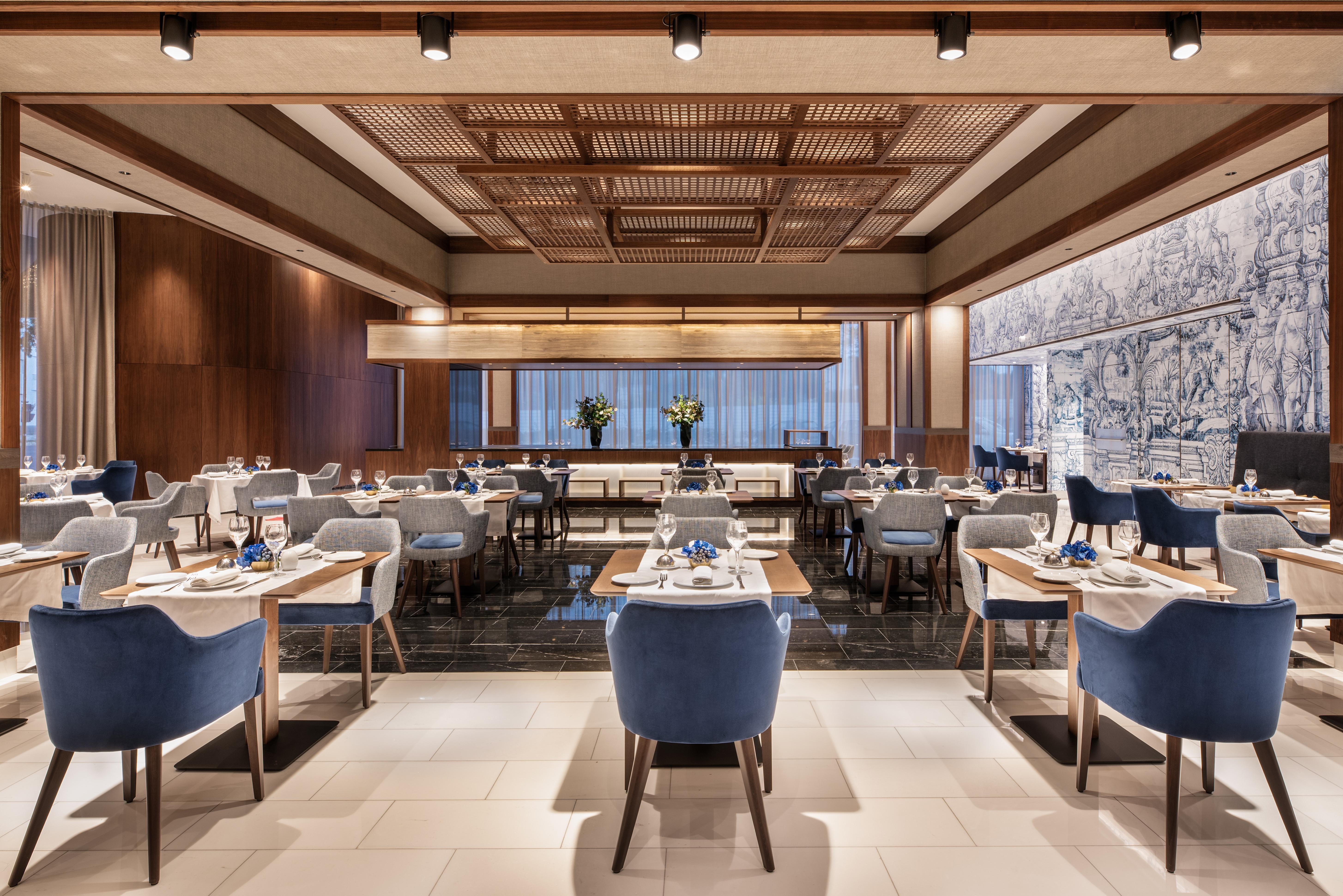 Eurostars Universal Lisboa Dış mekan fotoğraf The photo shows an interior view of a modern restaurant. The space features a contemporary design with a warm color palette, including wood paneling and elegant blue upholstered chairs. There are several tables set for dining, with white tablecloths 
