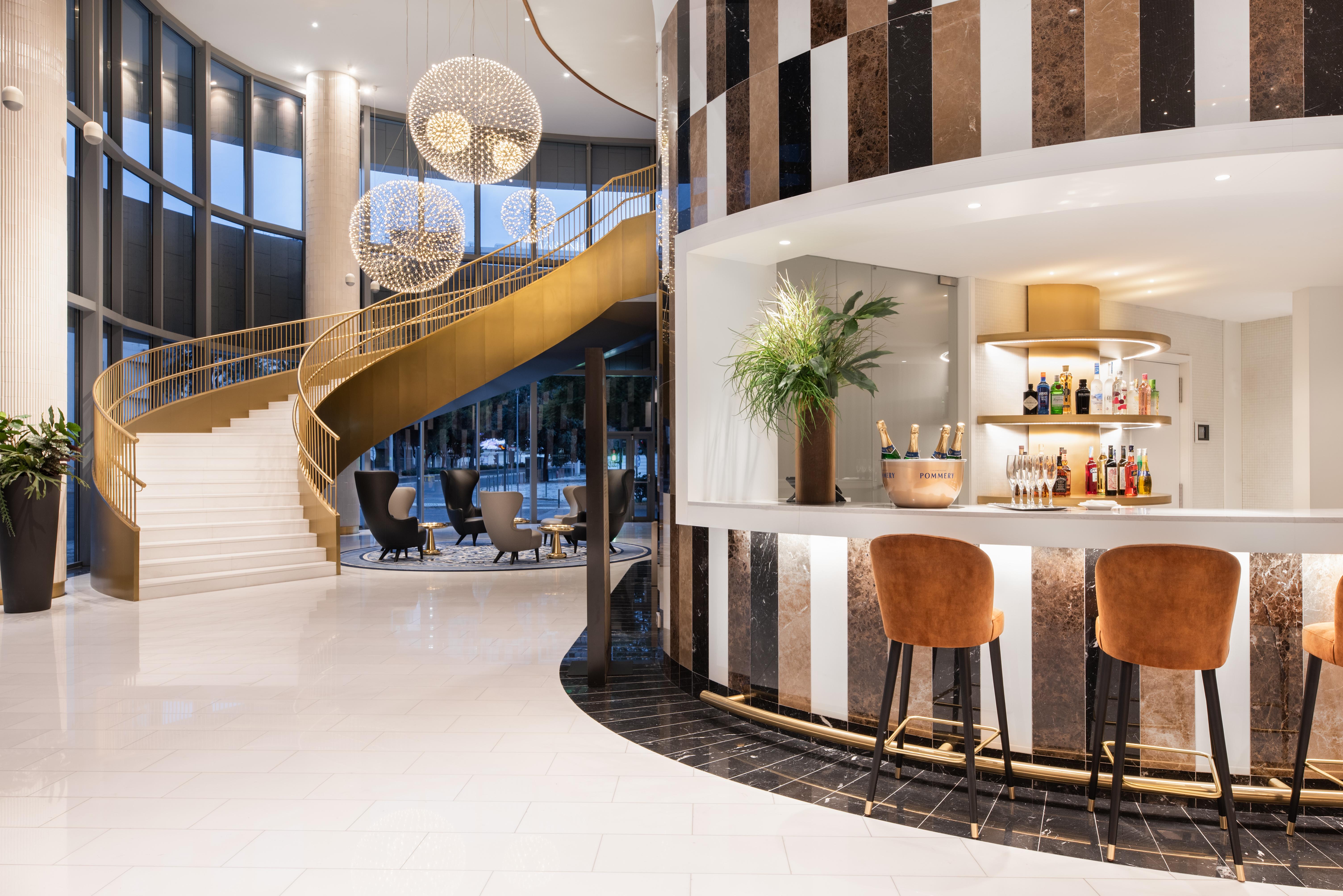 Eurostars Universal Lisboa Dış mekan fotoğraf The photo depicts a stylish, modern interior space featuring a curved staircase with a golden railing. The staircase leads to an upper level and is illuminated by large pendant lights. To the right, there is a sleek bar area with a white countertop, 