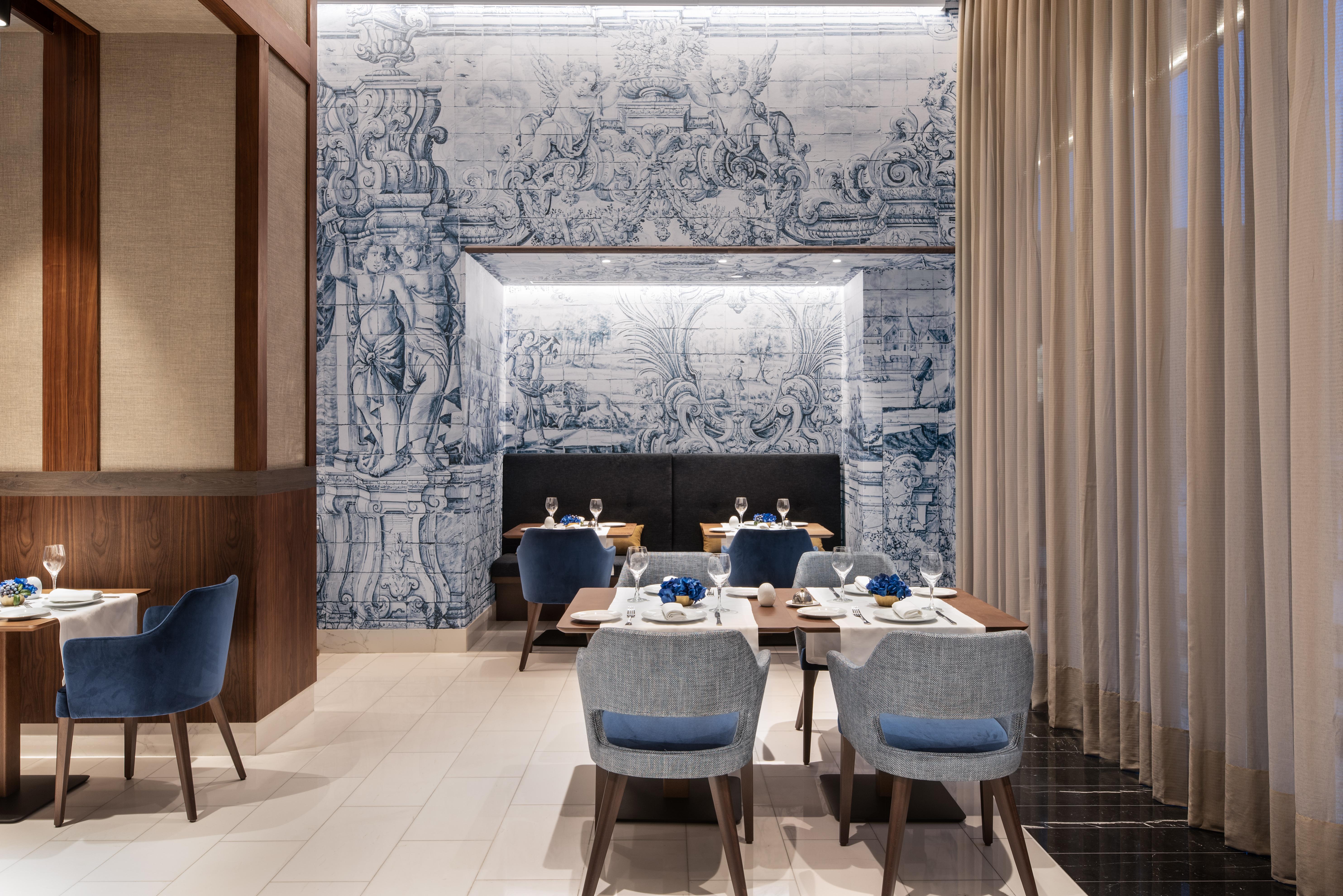 Eurostars Universal Lisboa Dış mekan fotoğraf The photo depicts an elegant dining area in a restaurant. The interior features modern furnishings with blue upholstered chairs and wooden tables. A striking mural, likely inspired by classical art, serves as a backdrop on one wall, featuring intrica