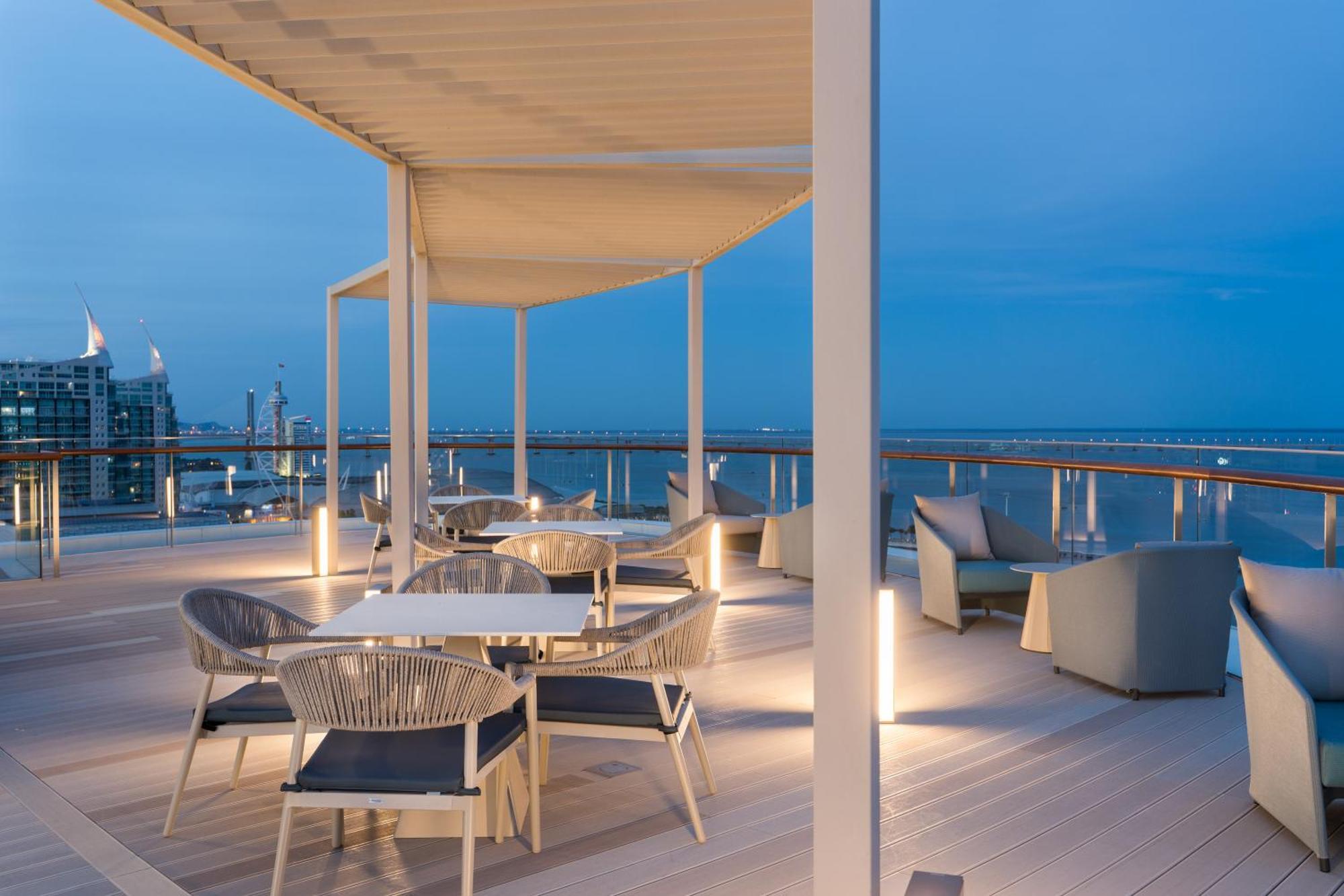 Eurostars Universal Lisboa Dış mekan fotoğraf The photo shows an outdoor seating area, likely on a balcony or terrace, with several white tables and chairs arranged neatly. The furniture features a modern design, with comfortable-looking chairs and minimalistic tables. There is a canopy structur