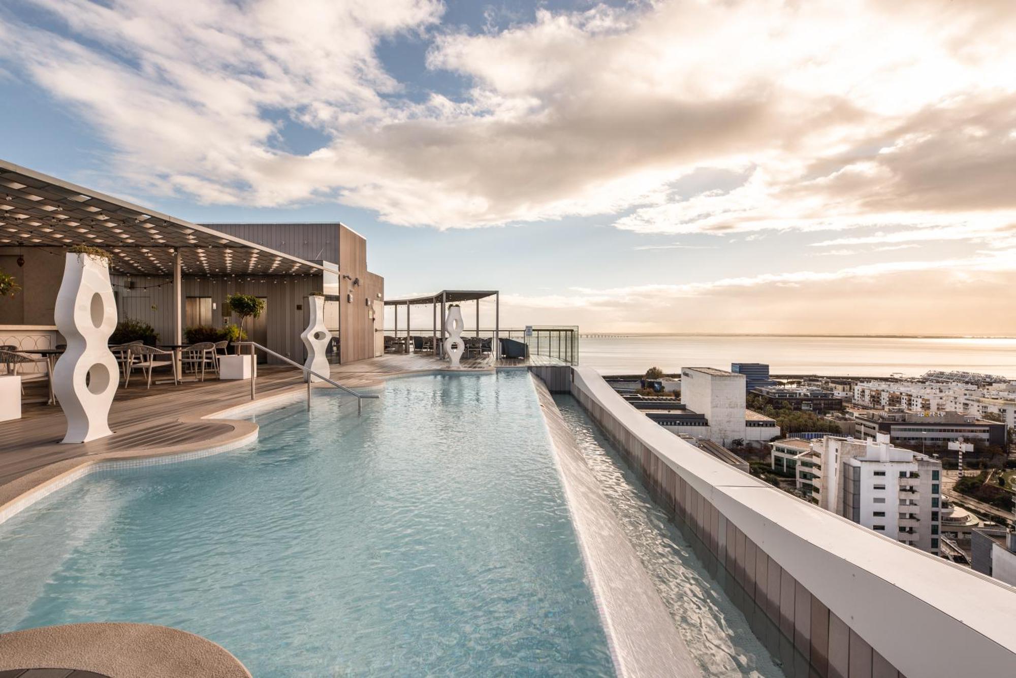 Eurostars Universal Lisboa Dış mekan fotoğraf The photo shows a rooftop infinity pool with a stunning view of the skyline and sea in the background. The pool features a sleek, modern design and extends towards the edge of the building, creating the illusion of water blending with the sky. Surrou
