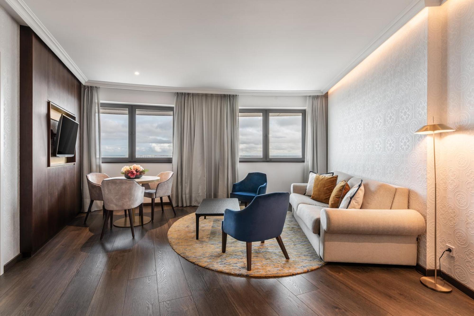 Eurostars Universal Lisboa Dış mekan fotoğraf The photo shows a modern and stylish hotel room or suite. It features a comfortable sofa in a light color, accompanied by two accent chairs—one blue and one a neutral tone. There’s a coffee table in front of the seating area, and a round rug undernea