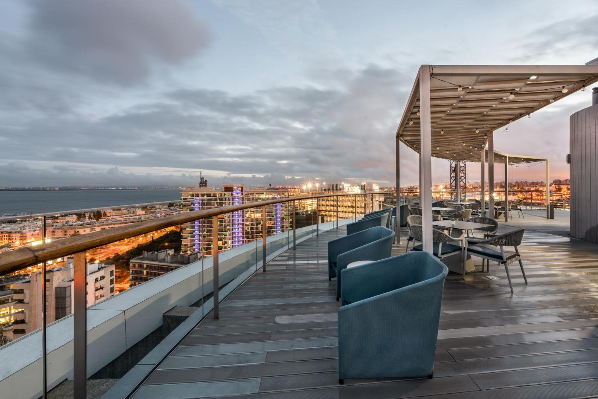 Eurostars Universal Lisboa Dış mekan fotoğraf The photo shows a rooftop terrace with a modern design. There are several blue chairs grouped around small tables, ideal for relaxation or dining. The terrace has a covered area which provides shade, and it overlooks a cityscape with buildings and a 