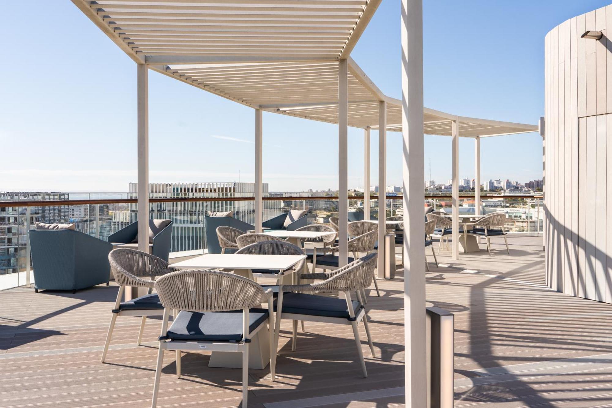 Eurostars Universal Lisboa Dış mekan fotoğraf The photo shows a rooftop terrace with a modern design. It features several covered seating areas with tables and chairs, arranged for dining or lounging. The furniture appears to be stylish and comfortable, with some matches of cushions and throws. 