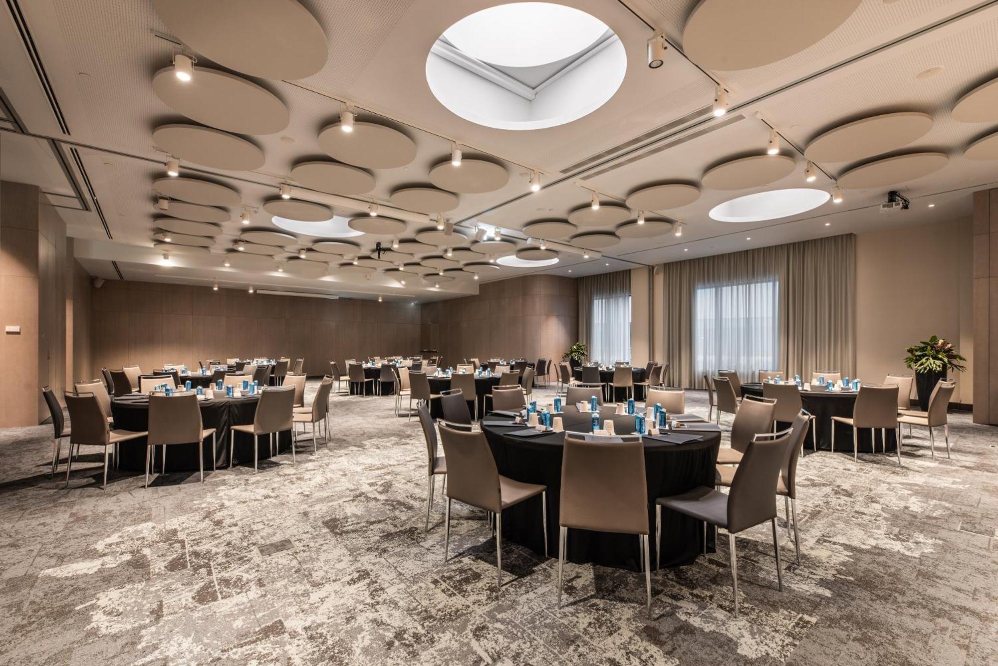 Eurostars Universal Lisboa Dış mekan fotoğraf The photo shows a spacious banquet room or conference hall. There are several round tables set up, each covered with black tablecloths and featuring light blue decorations or tableware. The room has a modern design, with a beige and soft gray color p