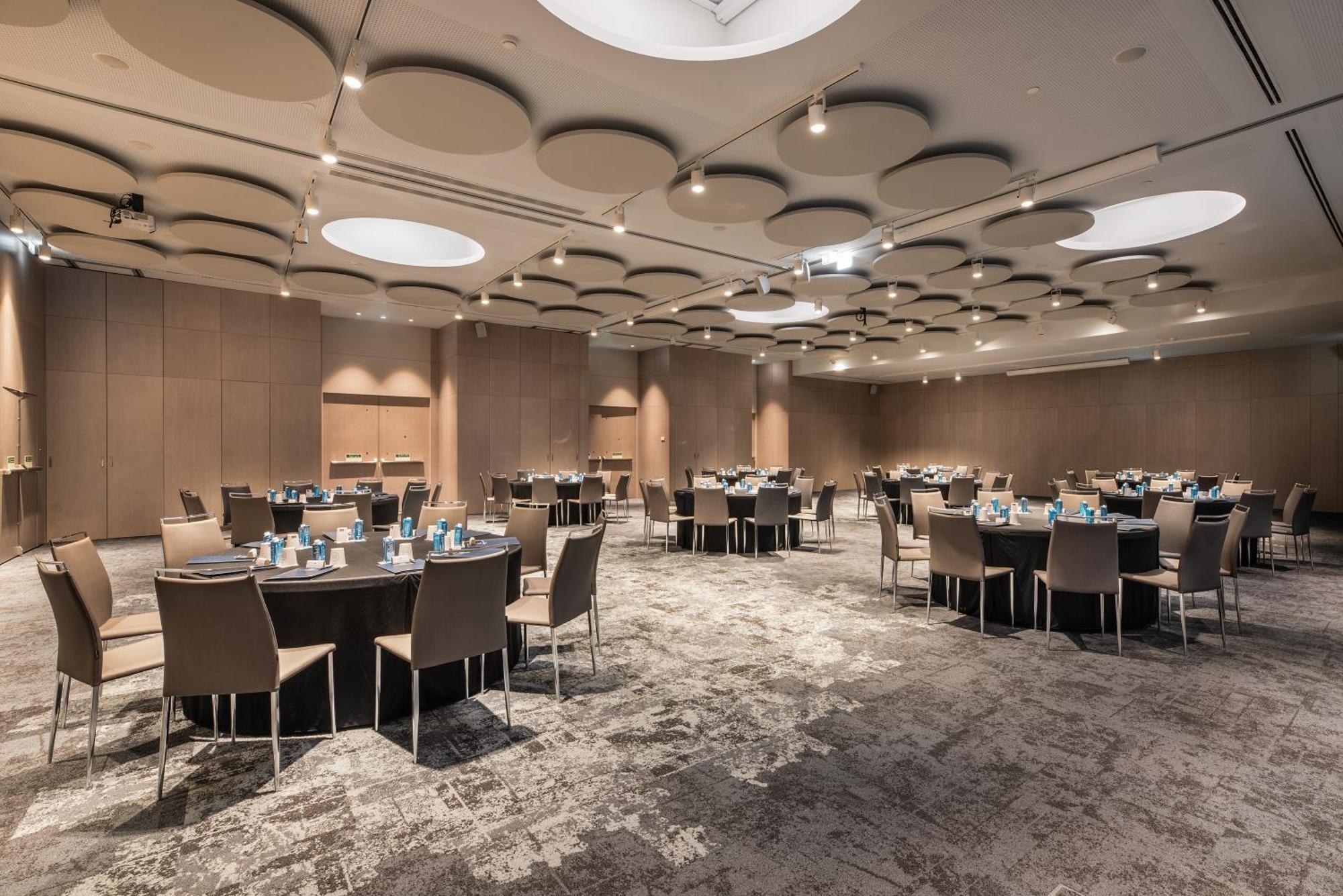 Eurostars Universal Lisboa Dış mekan fotoğraf The photo shows a spacious conference or banquet room. It features multiple round tables, each set with light blue tableware, indicating preparation for a dining or event setting. The room has modern decor with wooden paneling on the walls, and the c