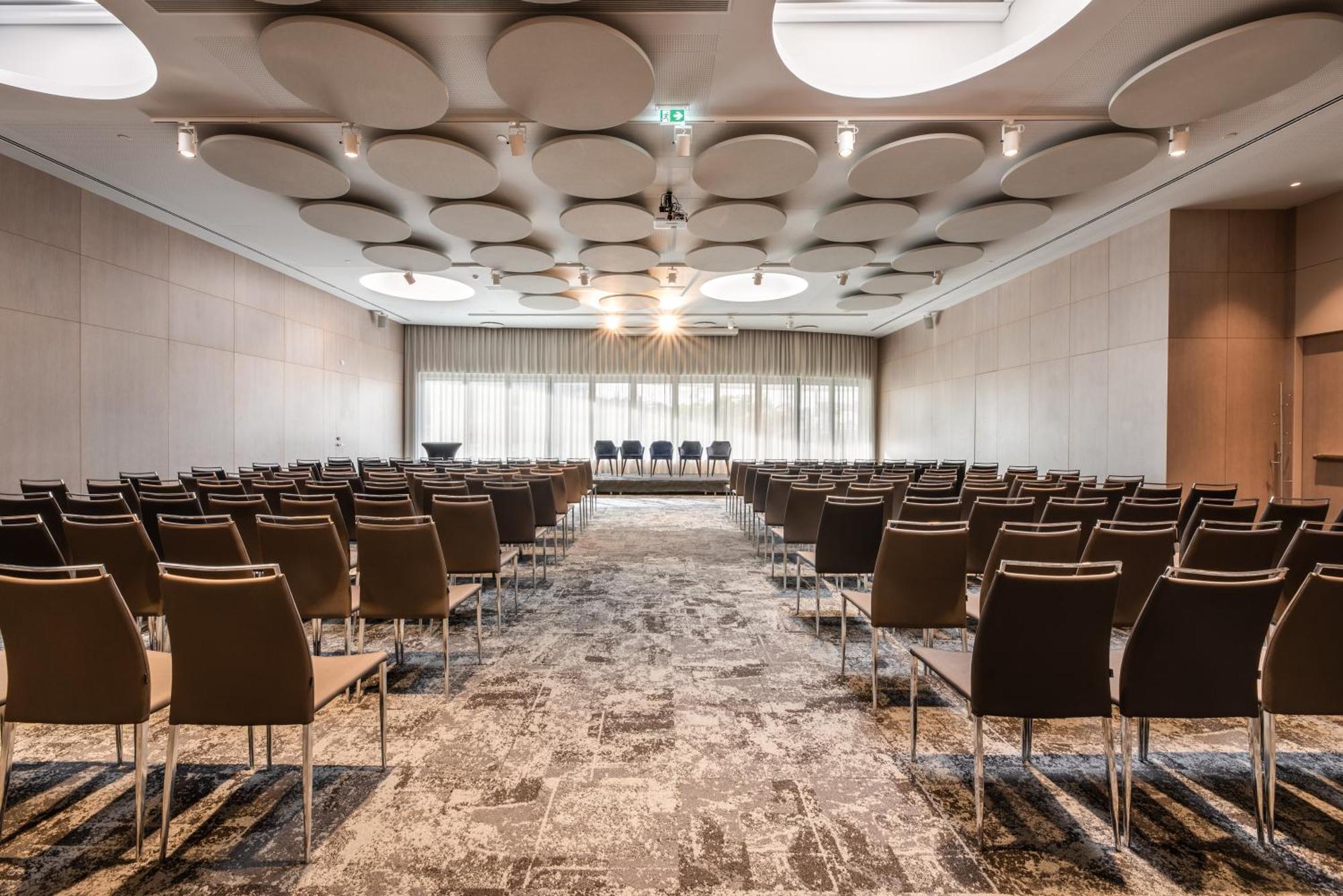 Eurostars Universal Lisboa Dış mekan fotoğraf The photo shows a conference or meeting room set up for an event. The room features rows of brown chairs arranged facing a small stage or presentation area at the front. The ceiling has a unique design with circular panels, adding an interesting arch